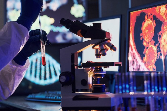 Monitors with information on the table. Scientist in white protective uniform works with coronavirus and blood tubes in laboratory.